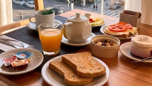 A breakfast tray with toast, fruit, tea, and a small container of nuts on a table by a window with a city view. - LM Hotel (Buenos Aires)