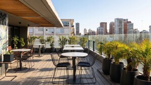 A rooftop terrace with tables and chairs, potted plants, and a city skyline view. - LM Hotel (Buenos Aires)