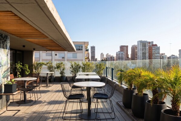 A rooftop terrace with tables and chairs, potted plants, and a city skyline view. - LM Hotel (Buenos Aires)