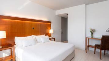 A hotel room with a large bed, bedside lamps, a desk with a chair, and a wooden headboard.