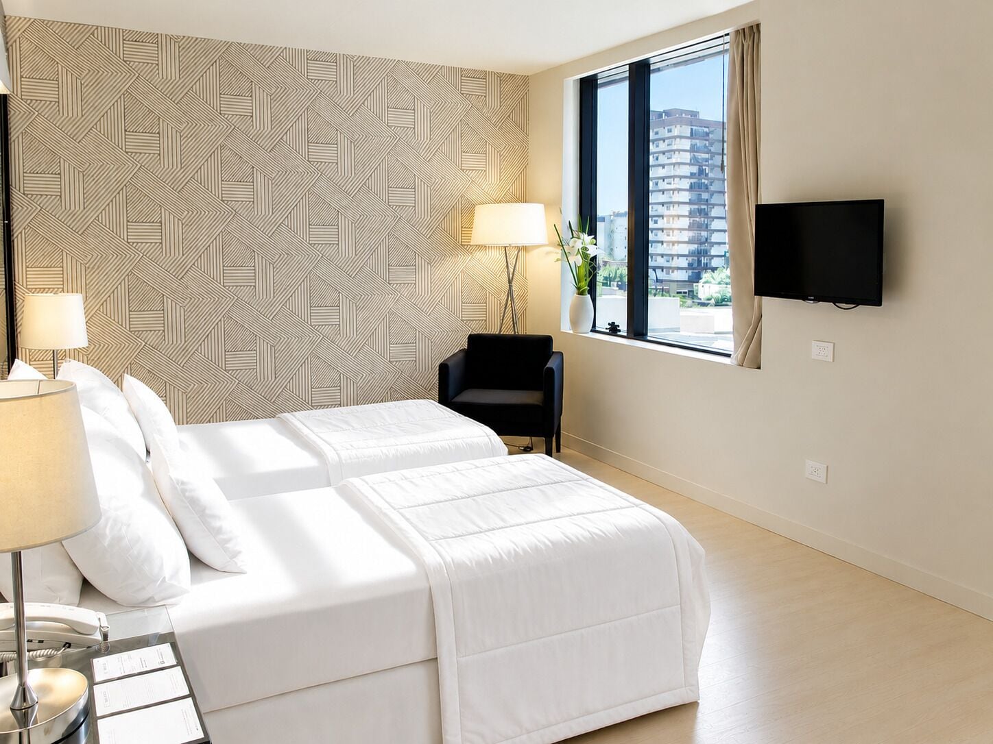Habitación de hotel con cama, mesitas de noche, lámpara, televisor y ventana con vista a edificios.