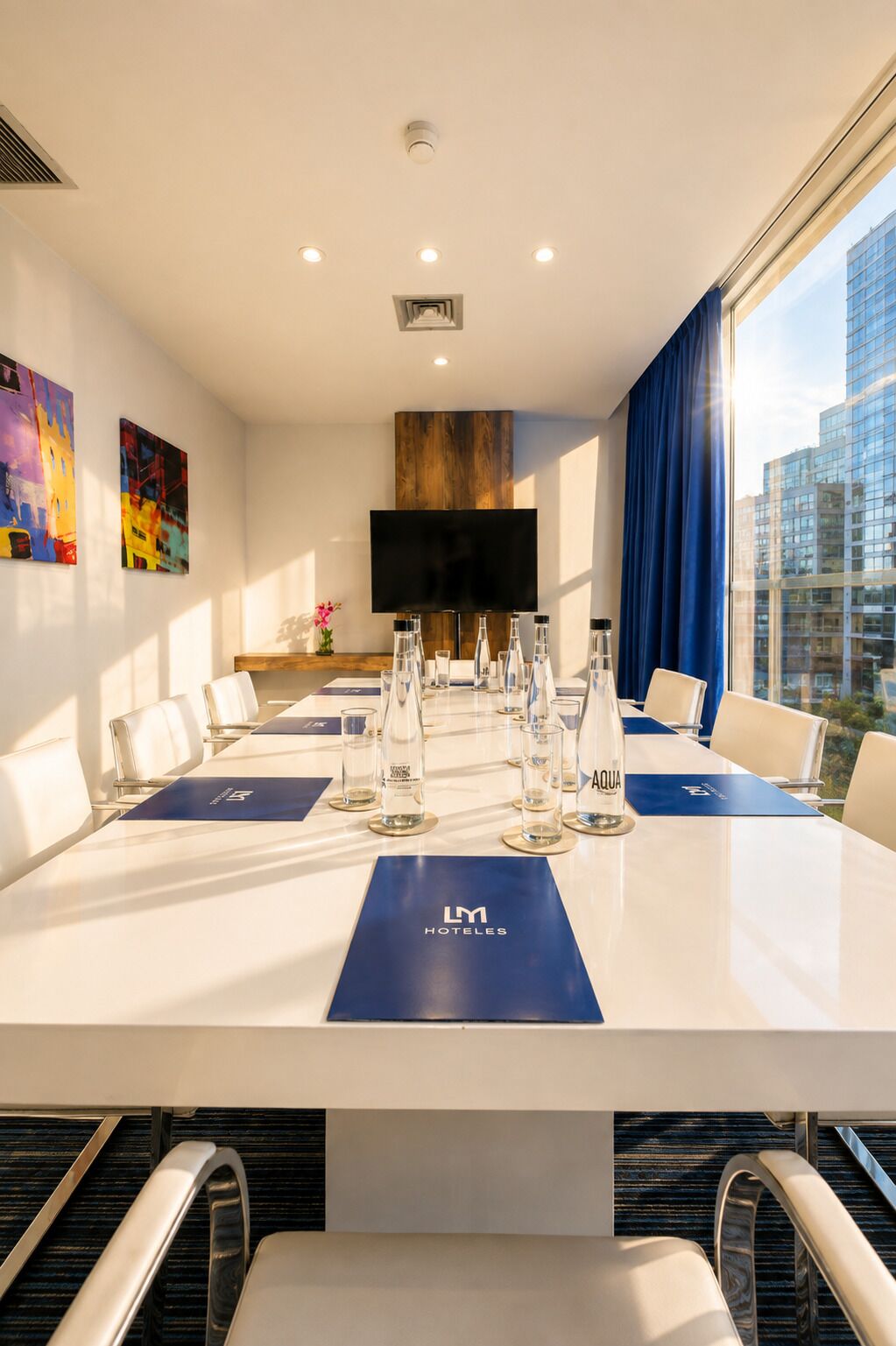 Un salón de conferencias con una larga mesa, sillas, un televisor de pantalla plana y vista a la ciudad.