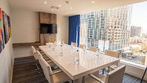 A conference room with a long table, chairs, bottles of water, a TV, and a city view. - LM Hotel (Buenos Aires)