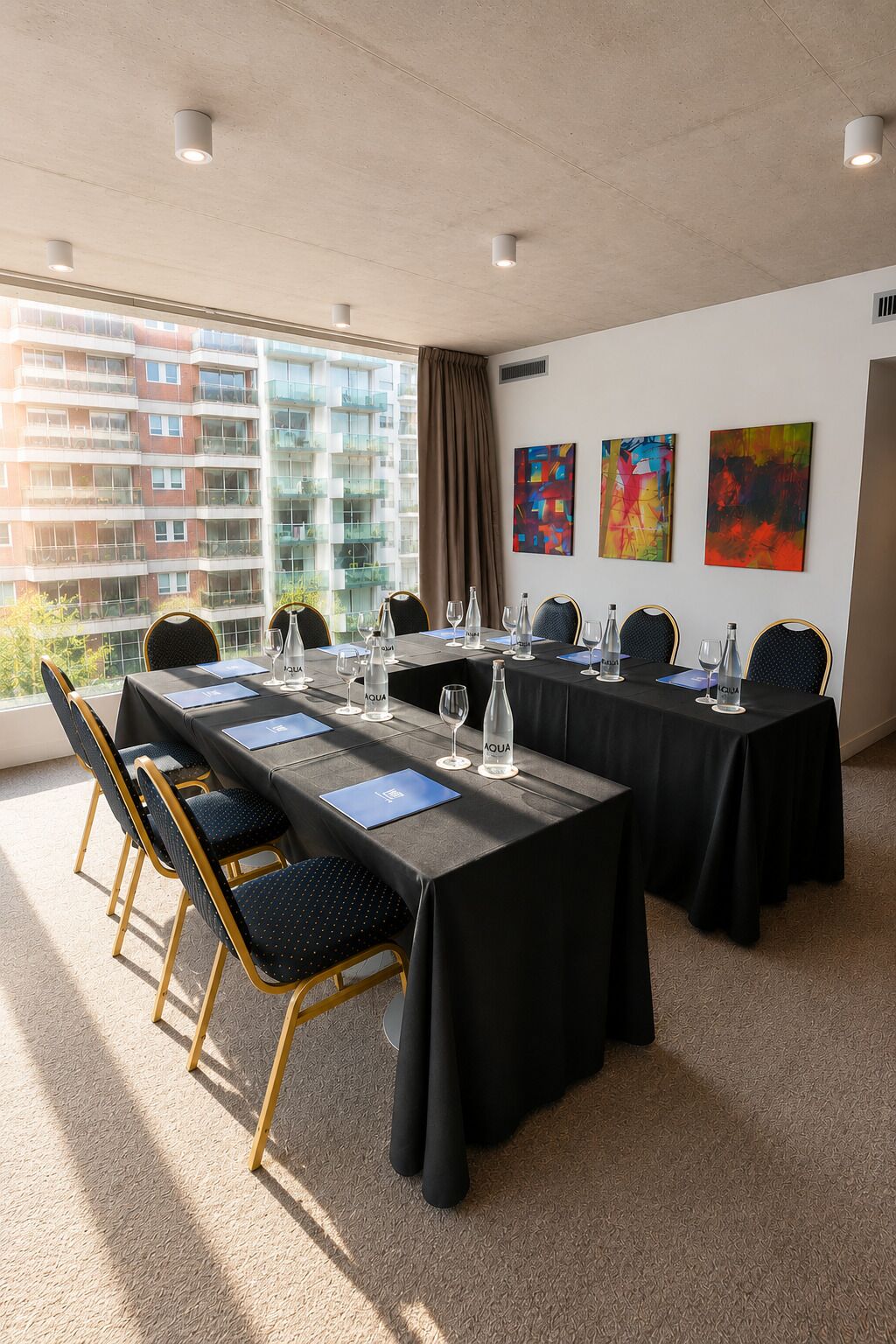 A conference room with a long table, chairs, and a view of a building through large windows.