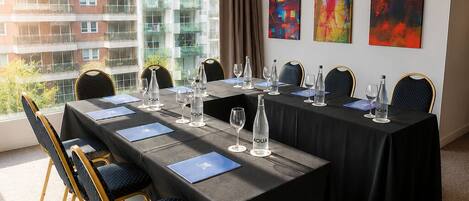 A conference room with a long table, chairs, and a view of a building through large windows.