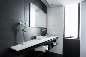 Un baño moderno con pared oscura, encimera blanca y un espejo grande.