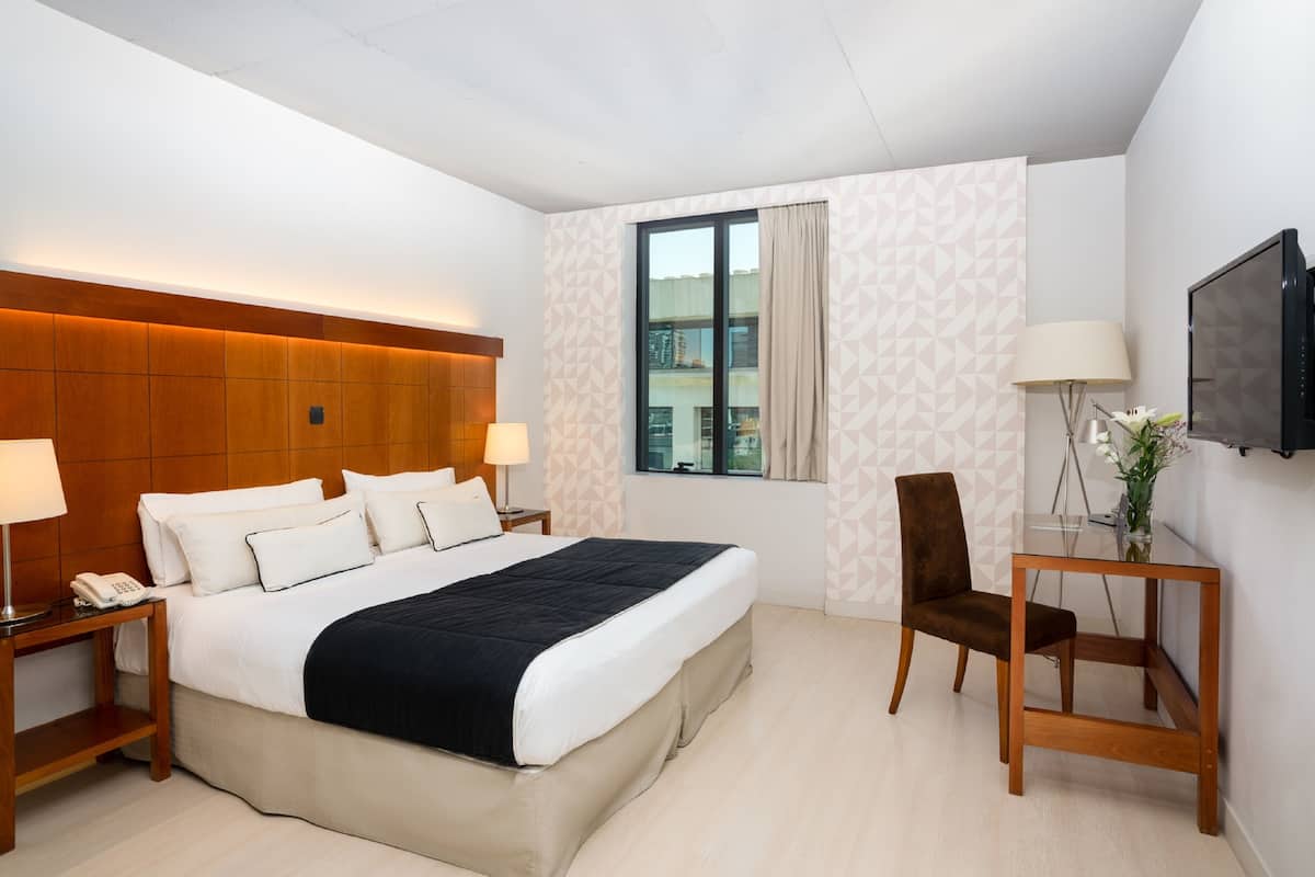 A hotel room with a large bed, a desk, a chair, a TV, and a window with curtains.