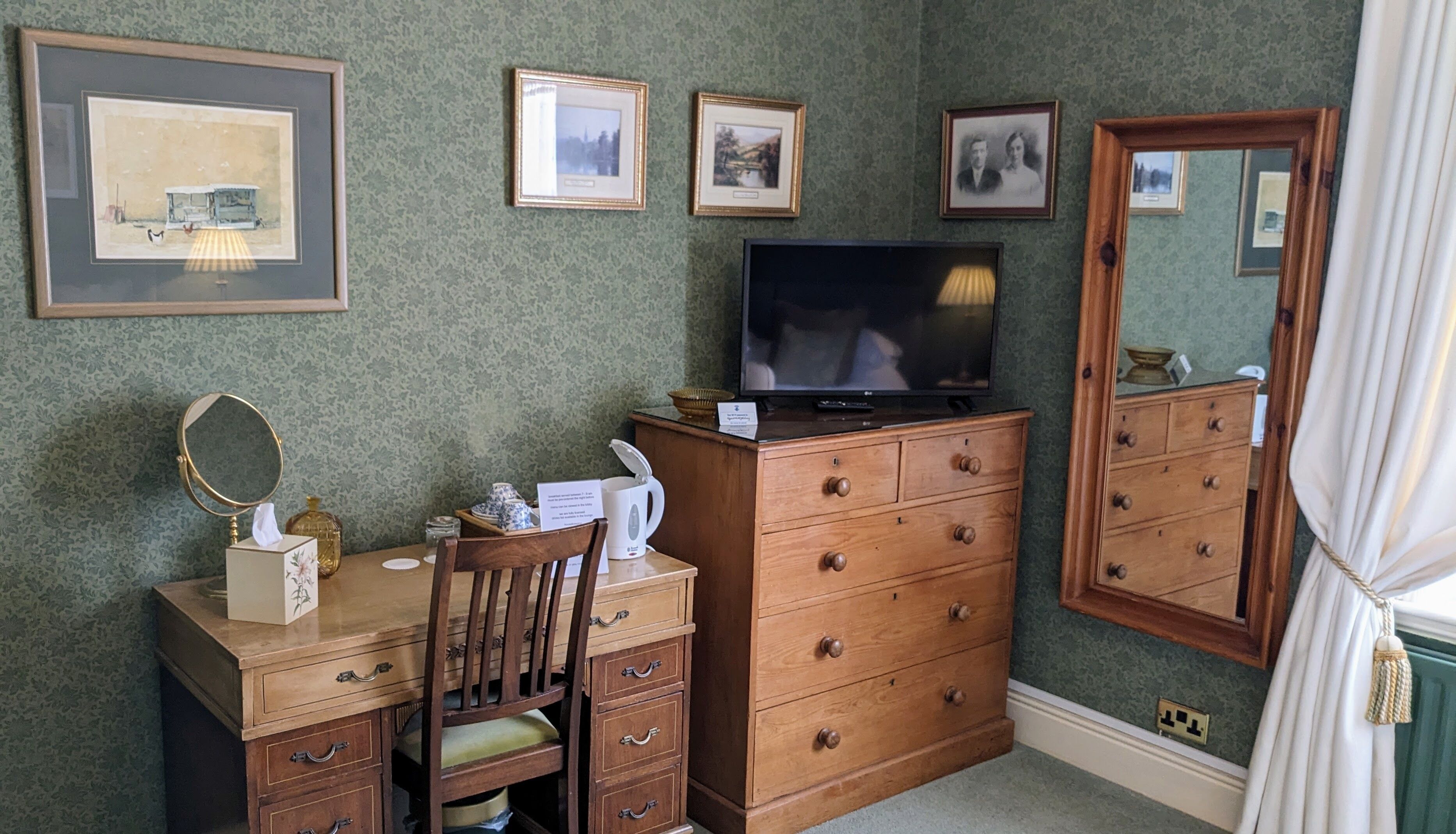 A room with a wooden dresser, a television, a mirror, and framed pictures on the wall.