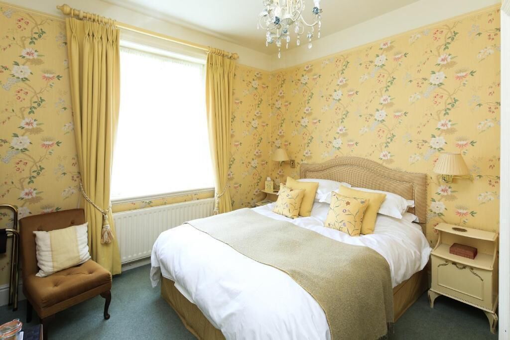 A bedroom with a large bed, a chair, a nightstand, and a window with curtains.