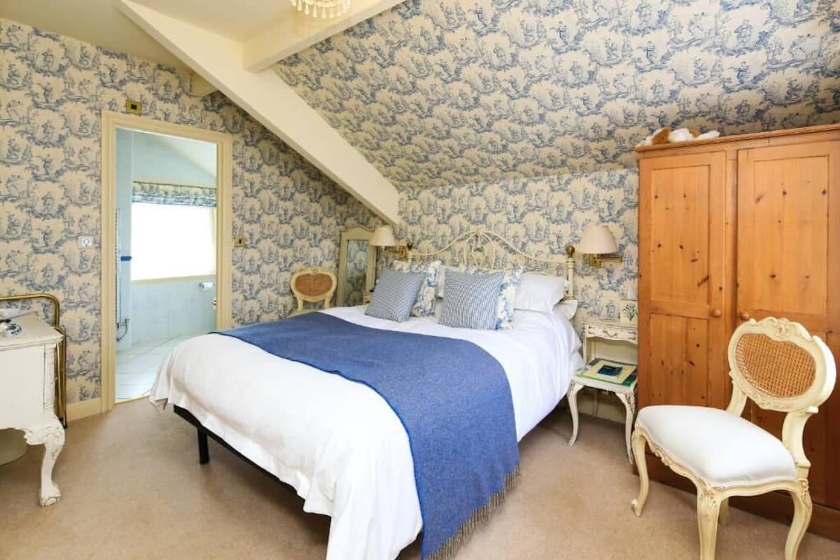 A bedroom with a bed, a wooden wardrobe, a chair, and a nightstand.
