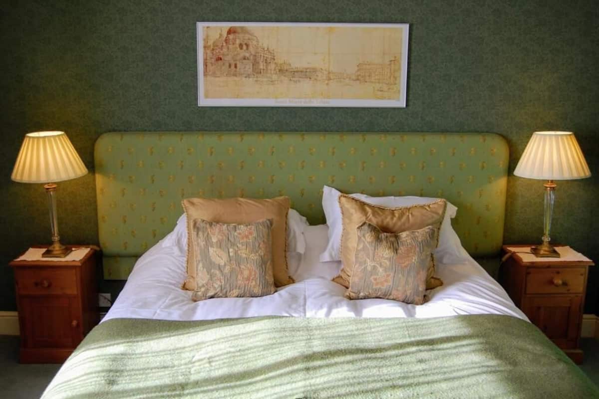 A bedroom with a green upholstered headboard, two bedside tables with lamps, and a framed picture on the wall.