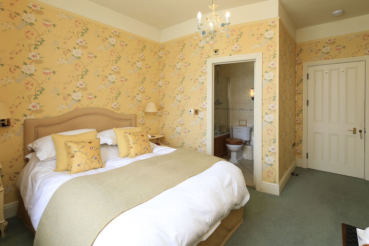 A bedroom with a large bed, floral wallpaper, a chandelier, and a door leading to a bathroom.