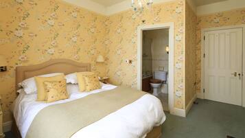 Un dormitorio con una cama grande, papel tapiz floral, un candelabro y una puerta que da a un baño.