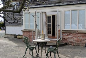 A patio with two green metal chairs and a table, a bottle of champagne, and a glass on the table. - The Old Vicarage Dolfor  (Newtown)