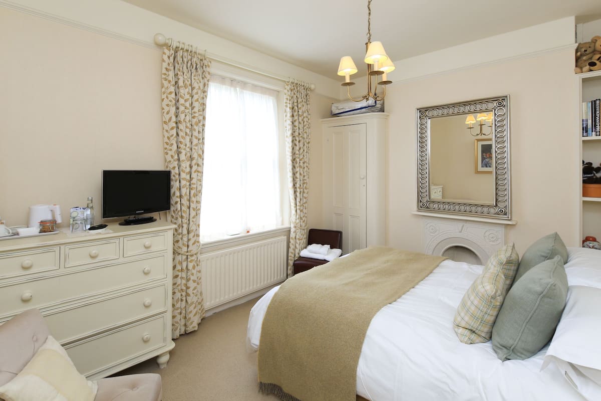 A hotel room with a bed, a dresser, a television, a mirror, and a fireplace.