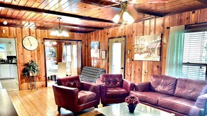 A cozy living room with wooden walls, leather sofas, a glass coffee table, and a dining area visible through an open door. - 4BR, 4BA House Beach, Entertainment, Nightlife (Hollywood)