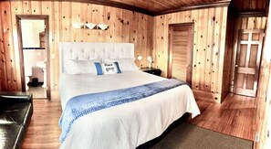A bedroom with a large bed, wooden walls, a bedside table, and a nightstand.