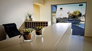 Un espacio de oficina moderno con una mesa grande, dos plantas en macetas y vistas a una piscina al aire libre.