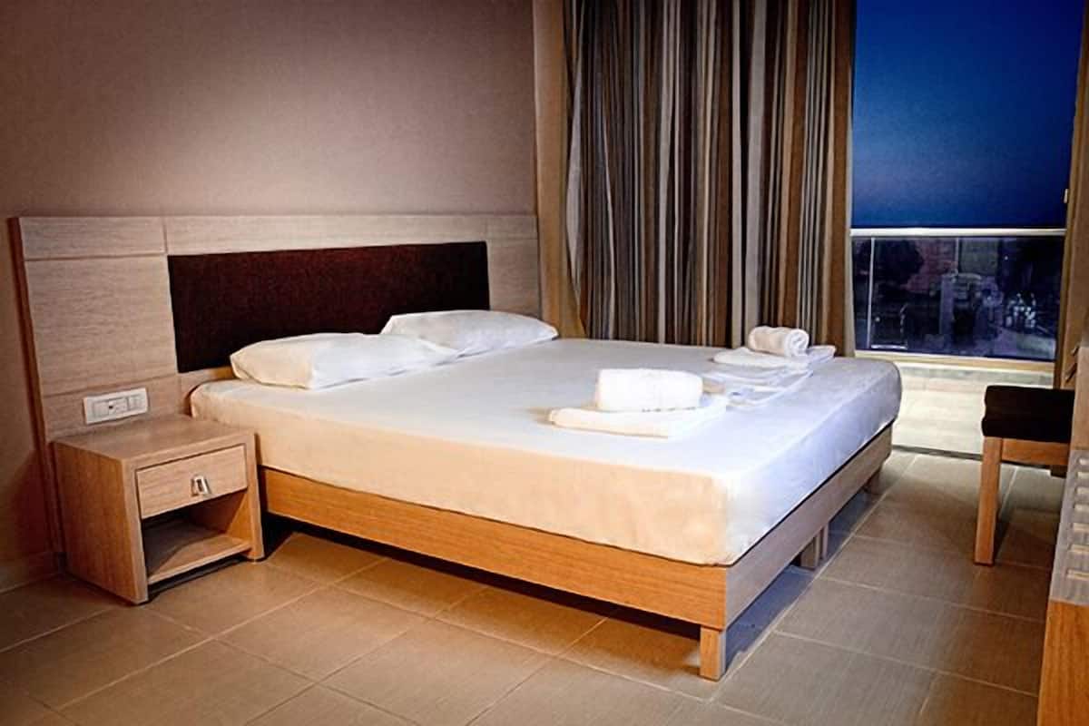 A hotel room with a large bed, a nightstand, a chair, and a window with curtains.