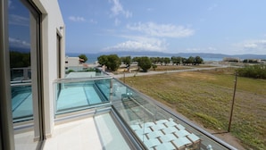 Un edificio moderno con balcón de vidrio que da a una piscina y una vista panorámica del mar y montañas distantes.