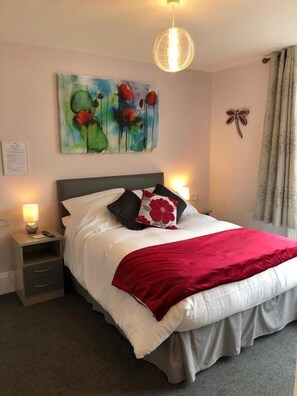 A bedroom with a bed, bedside tables, a painting, and a chandelier. - High Ways House (Ilfracombe)