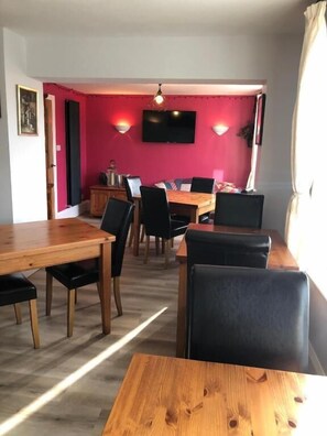 A dining area with a wooden table and chairs, a television mounted on the wall, and a red accent wall. - High Ways House (Ilfracombe)