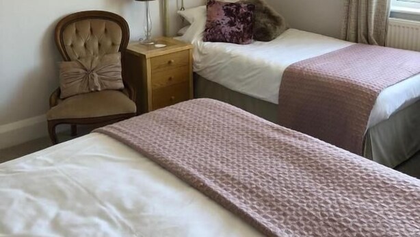 A bedroom with two beds, a nightstand, a chair, and artwork on the walls. - High Ways House (Ilfracombe)