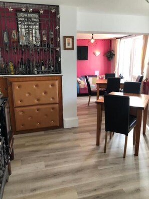 A dining area with a wooden table and chairs, a red accent wall, and a decorative metal gate. - High Ways House (Ilfracombe)