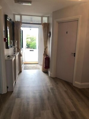 A hallway with a door, a radiator, a mirror, and a window with curtains.