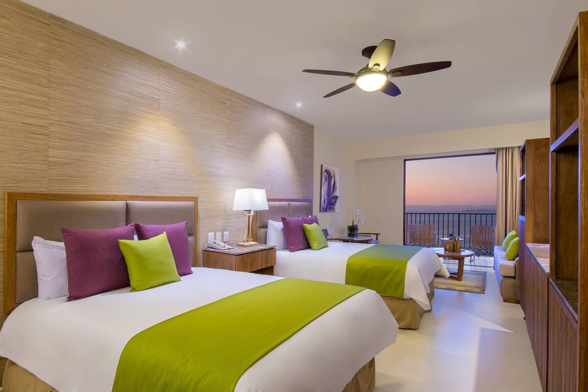 Habitación de hotel con dos camas, un balcón con vistas y un ventilador de techo.