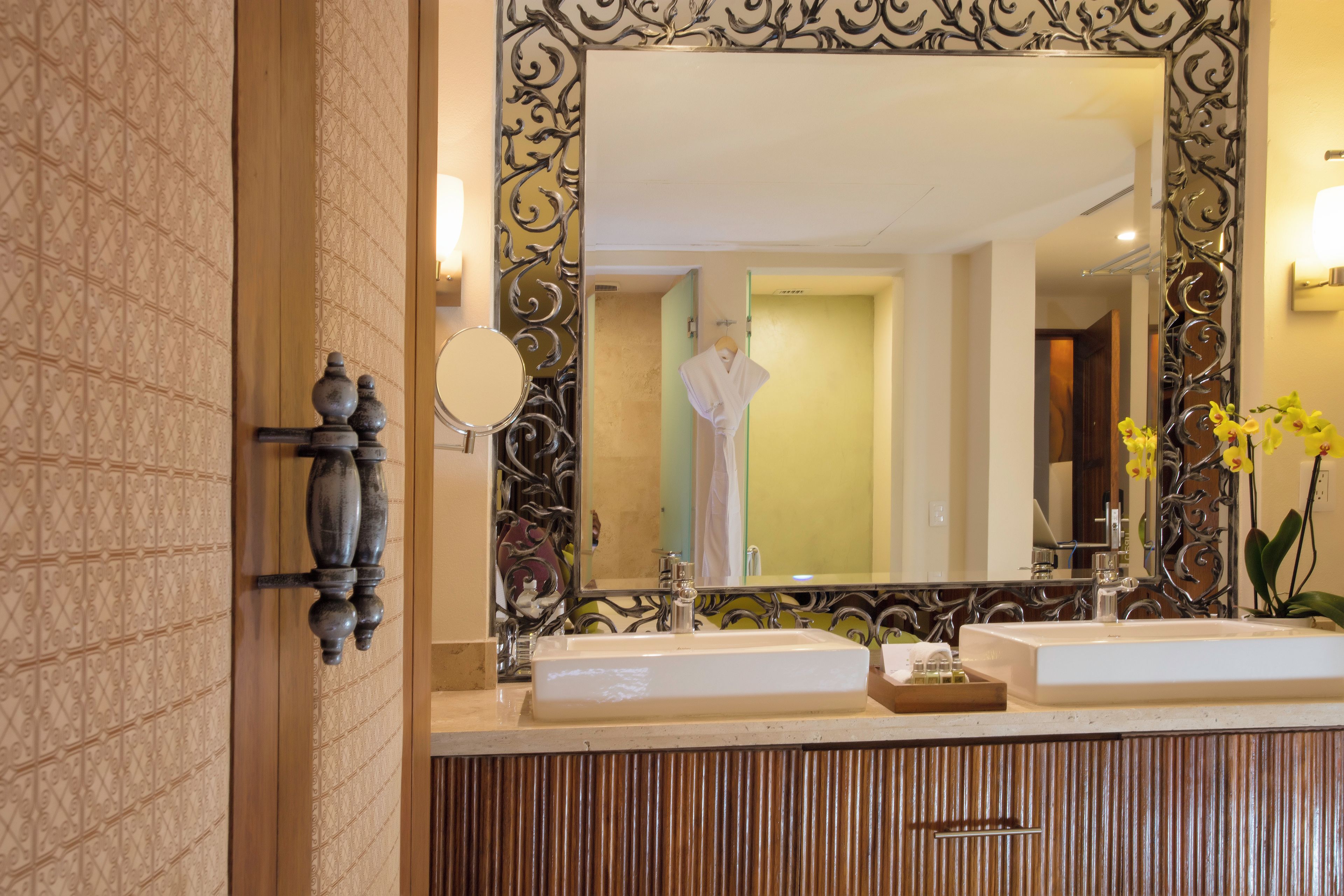 Un baño con dos lavamanos, un espejo con ornamentada estructura de metal y un perchero para toallas.