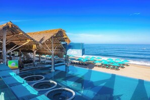 Ein Infinity-Pool mit Blick auf den Strand, Hütten mit Reetdach und Liegestühle mit Sonnenschirmen.