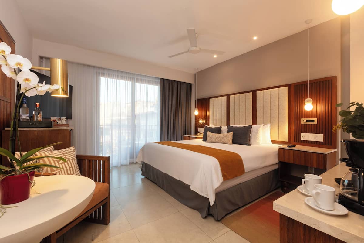 Una habitación de hotel moderna con una cama grande, un escritorio con dos tazas, una cafetera y una planta en maceta.