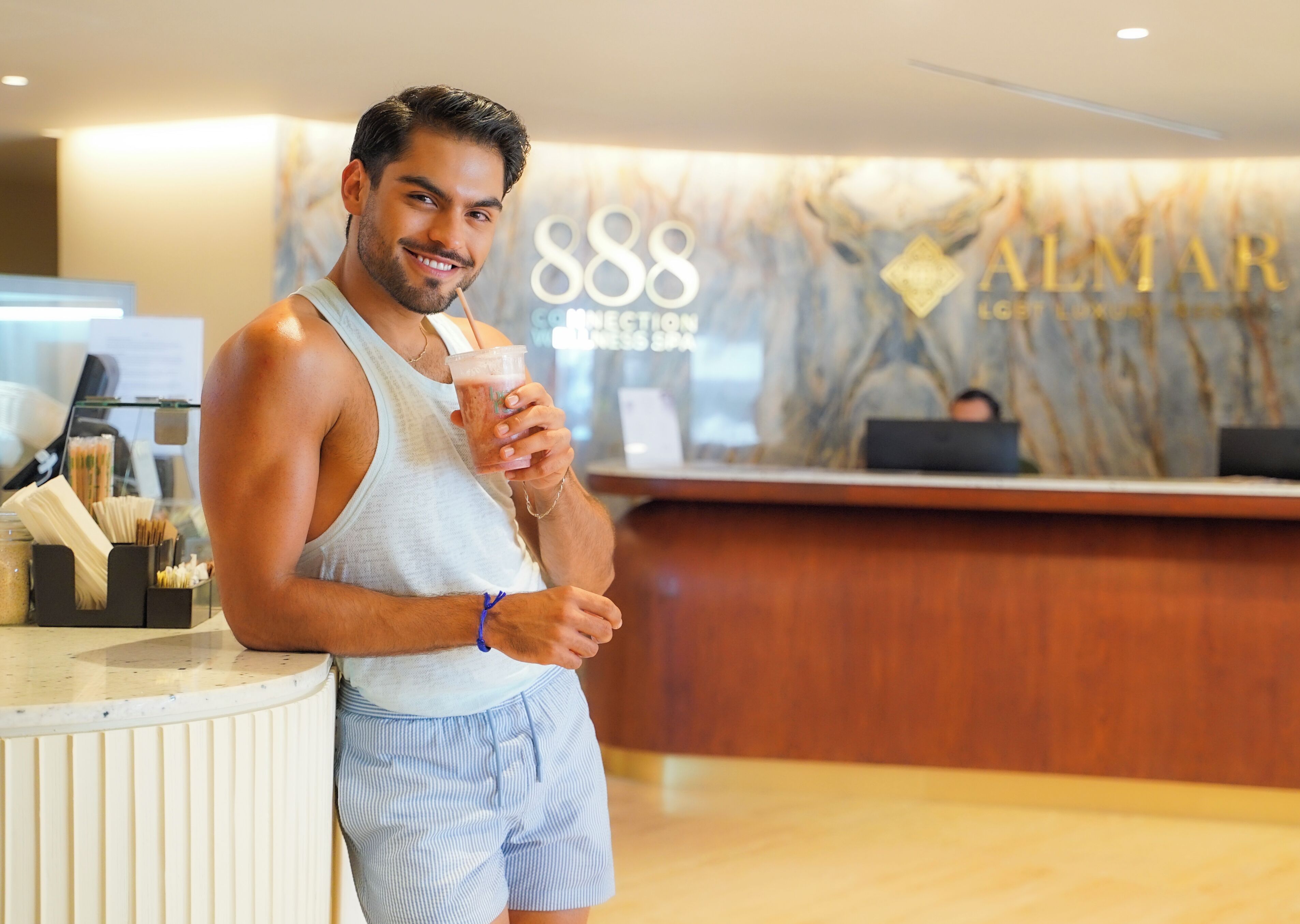 A man in a hotel lobby holding a drink, with a reception desk and a sign reading '888 Connect London' in the background.