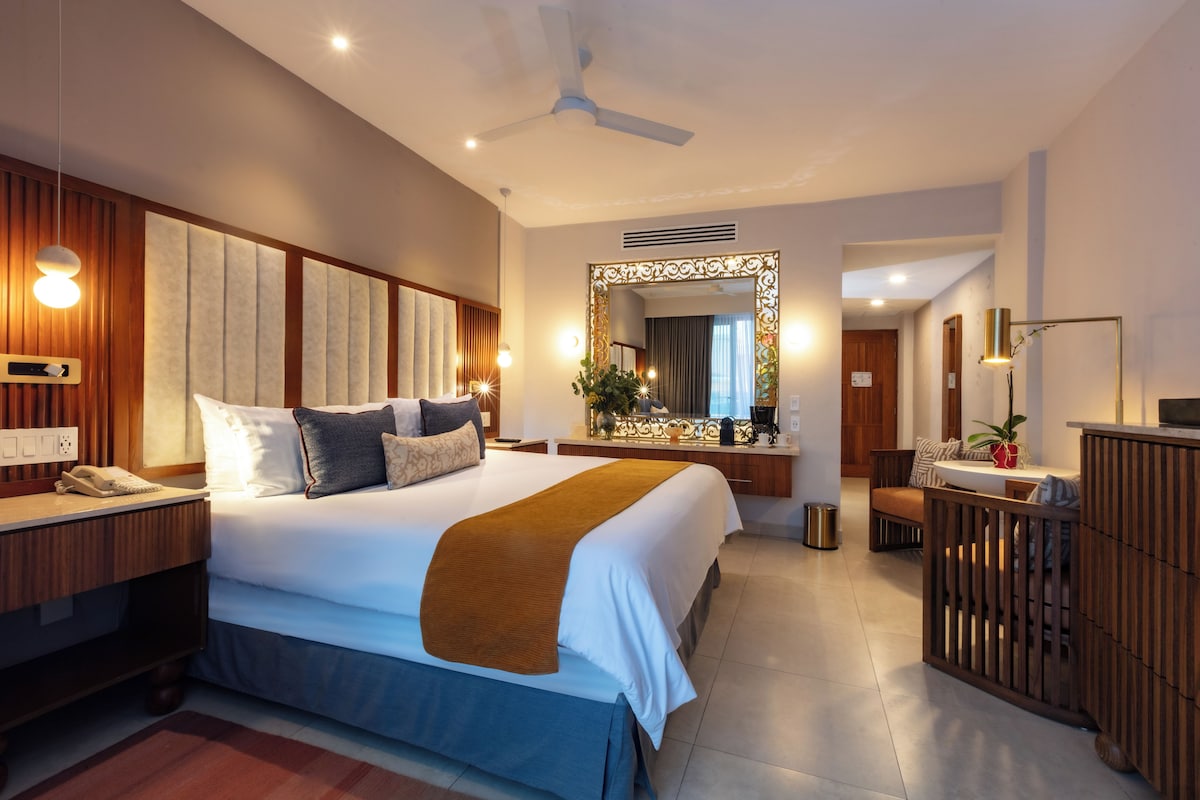 Una habitación de hotel moderna con una cama grande, mesita de noche y un espejo.