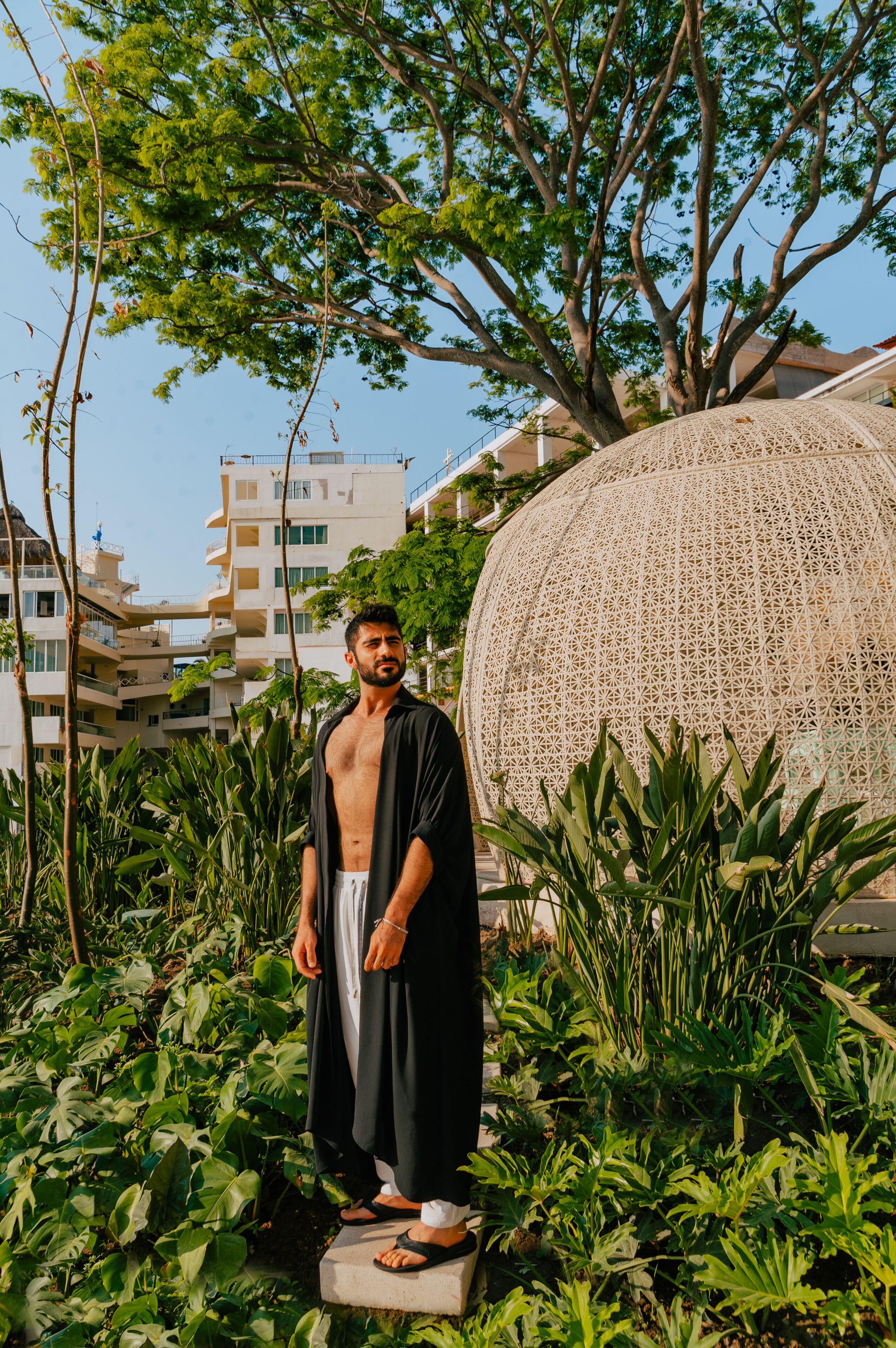 A man standing in a garden with a large decorative sphere and buildings in the background.
