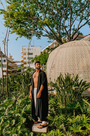 A man standing in a garden with a large decorative sphere and buildings in the background.