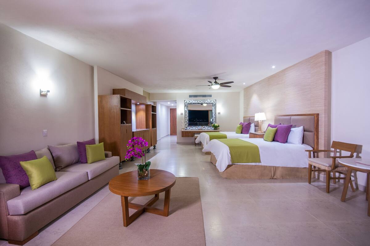 Habitación de hotel con sofá, dos camas, una mesa de comedor y ventilador de techo.