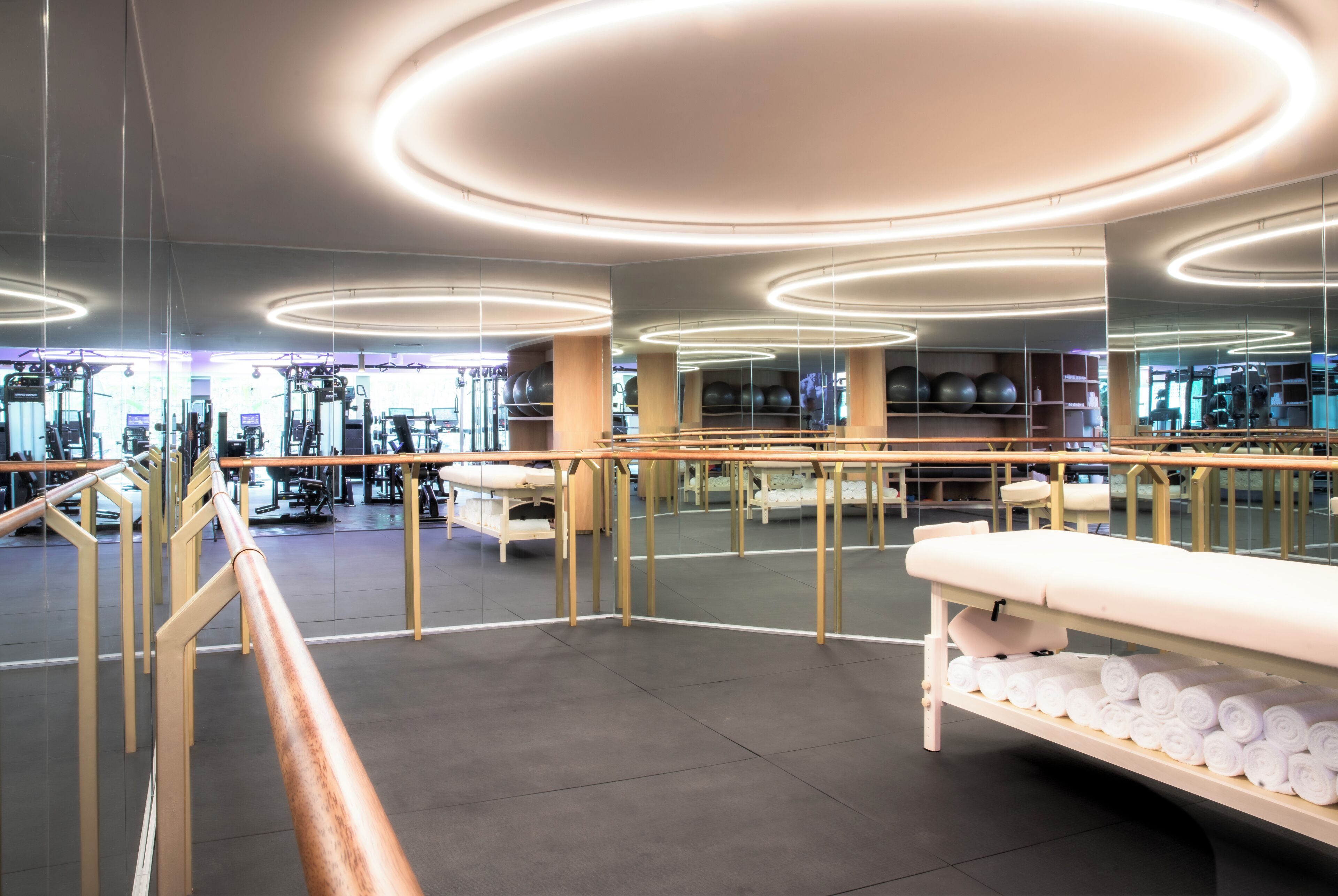 A modern gym with exercise equipment, a reception desk, and a large mirror reflecting the space.