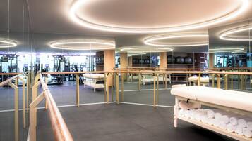 A modern gym with exercise equipment, a reception desk, and a large mirror reflecting the space.