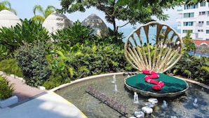 A pool area with a water feature, a chair, and lush greenery.