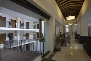 A spacious lobby with a wooden floor, a glass railing, and a seating area with chairs and a sofa.