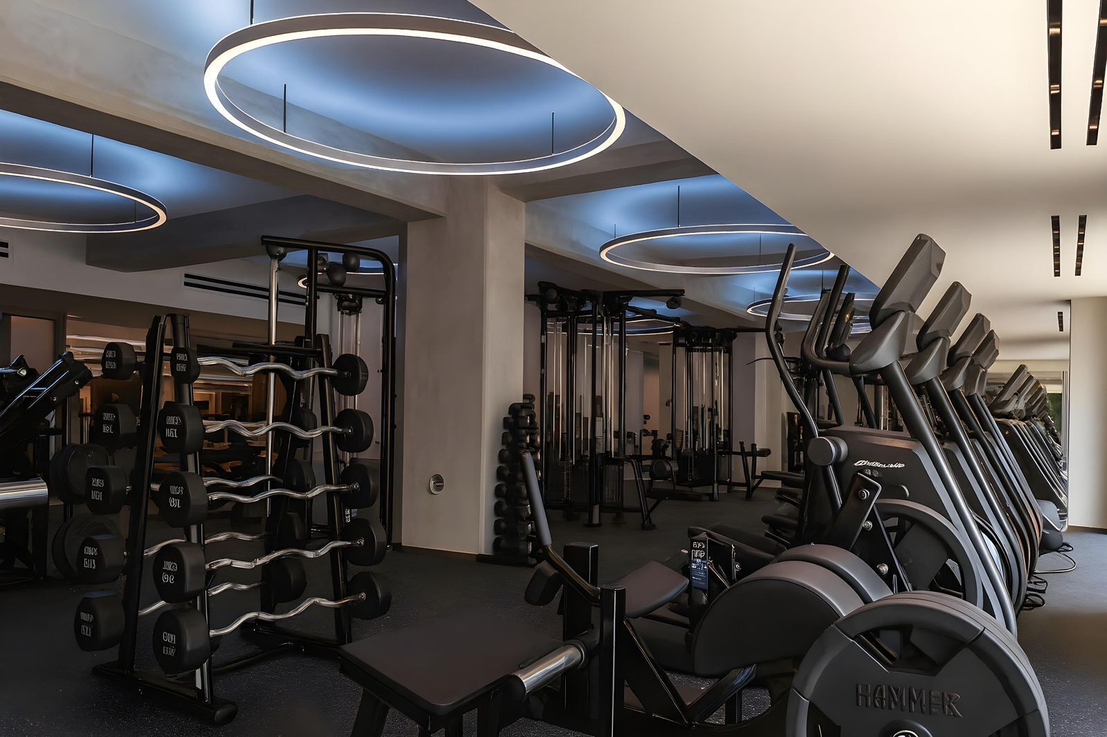 Ein modernes Fitnessstudio mit verschiedenen Trainingsgeräten, darunter Kurzhanteln, Kraftgeräte und Laufbänder.
