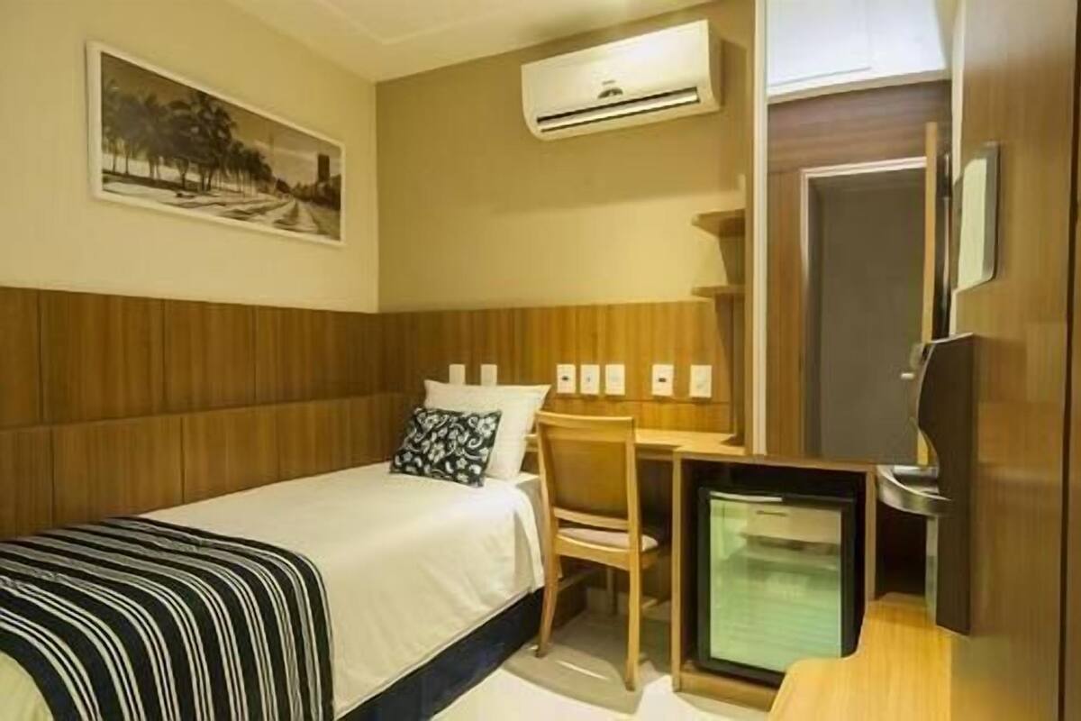 Ein Hotelzimmer mit Bett, Schreibtisch, Stuhl, Fernseher und Klimaanlage.