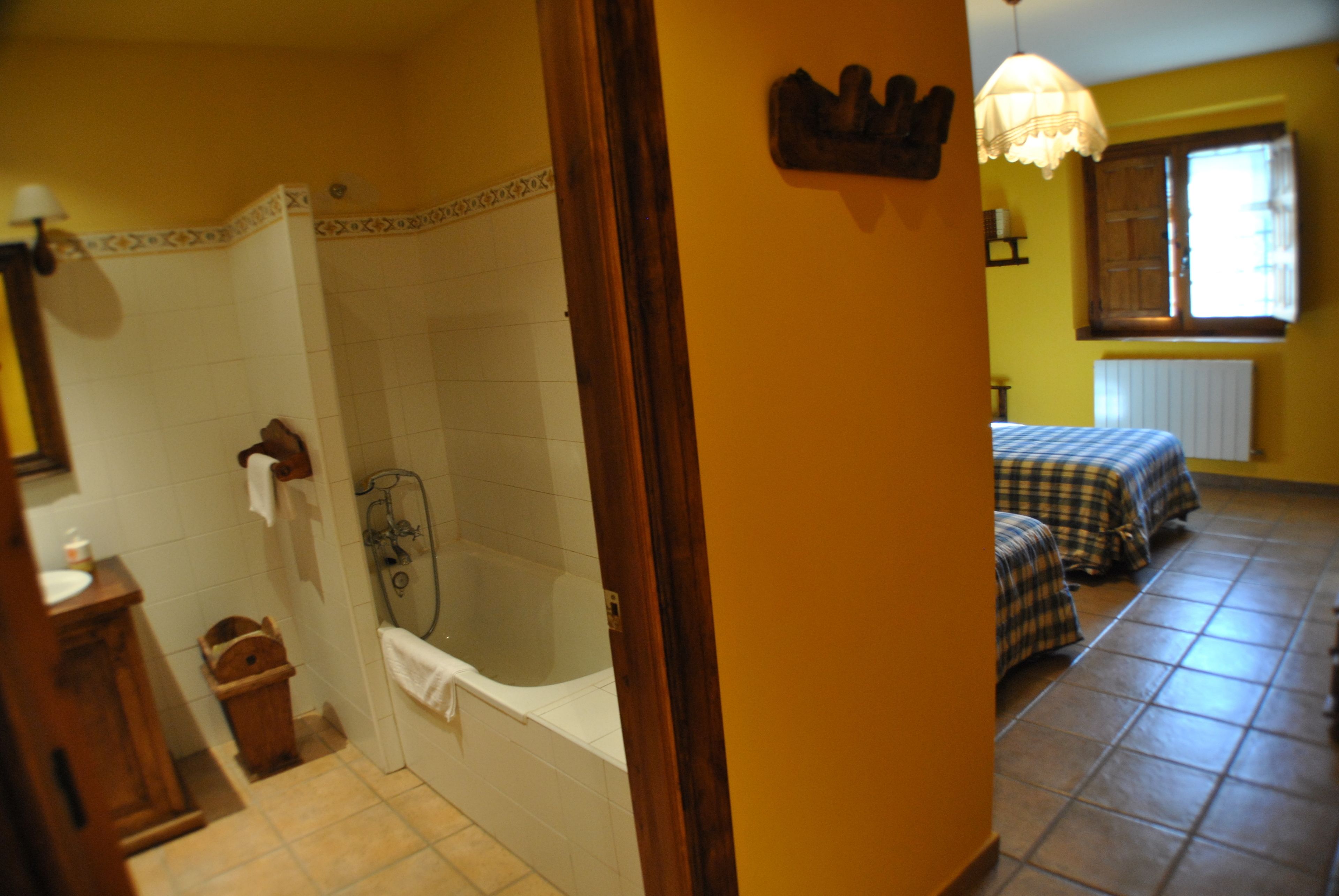 A bathroom with a bathtub, a shower, and a toilet. There is a wooden cabinet and a towel hanging on the wall.
