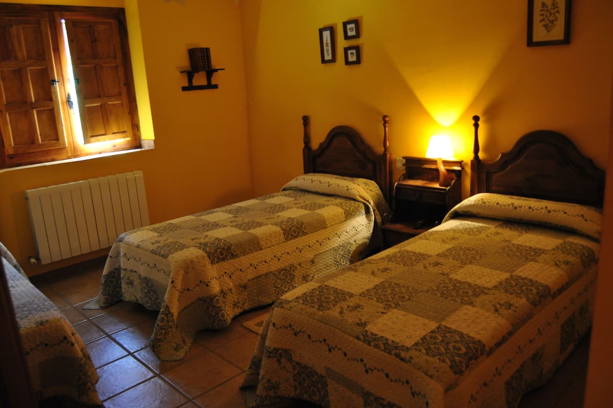 A room with two single beds, a wooden wardrobe, a radiator, and a window with wooden shutters.