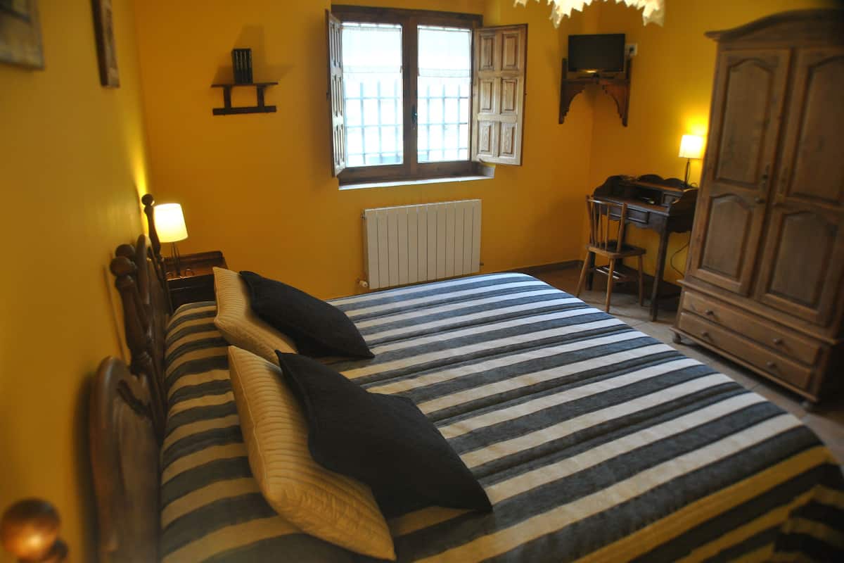A bedroom with a bed, a desk, a chair, a radiator, and a window with shutters.