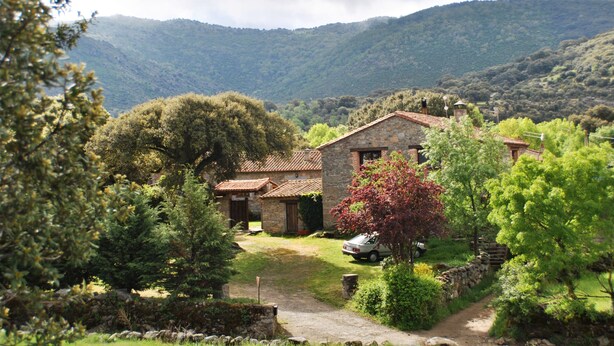 A stone house with a red-tiled roof, surrounded by lush greenery and a mountain backdrop. - La Trocha de Hoyorredondo (Hoyorredondo)