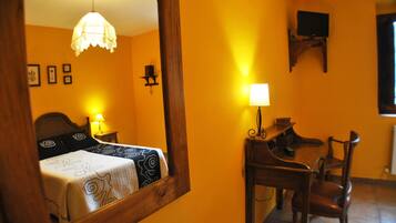 Une pièce comprenant un lit, un bureau, une chaise, un miroir, une lampe et un téléviseur fixé au mur.