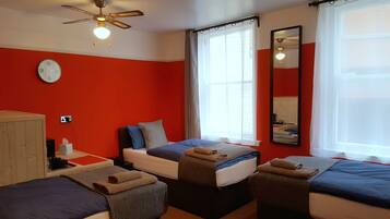 A hotel room with a red wall, a bed with a blue bedspread, a bedside table, a mirror, and a window with curtains.